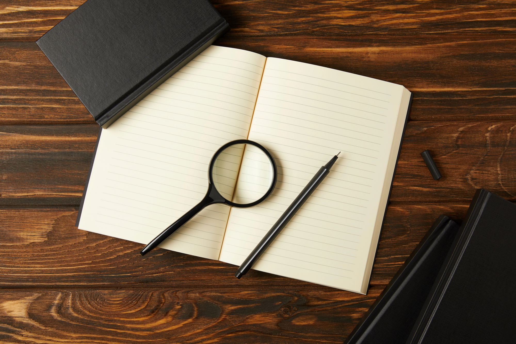 Top view of magnifying glass, notebooks, and pen on wooden table
