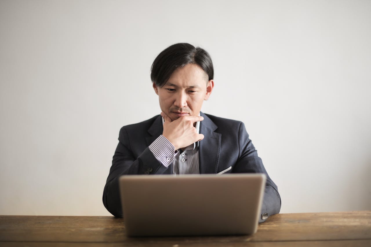 Self-Manage or Hire Amazon Sponsored Products Management Businessman looking at laptop, contemplating whether to self-manage or hire an Amazon Sponsored Products management agency for better ad performance.