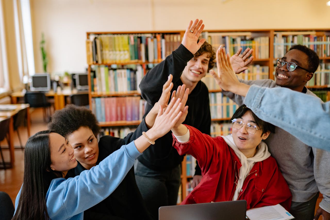 College Student Financial Welness A group of college students giving each other a high five, symbolizing strong teamwork and support, representing how successful college student financial wellness programs integrate multiple financial