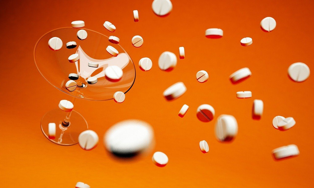White round tablets falling around and into a tilted martini glass against a bright orange background, with some motion blur.
