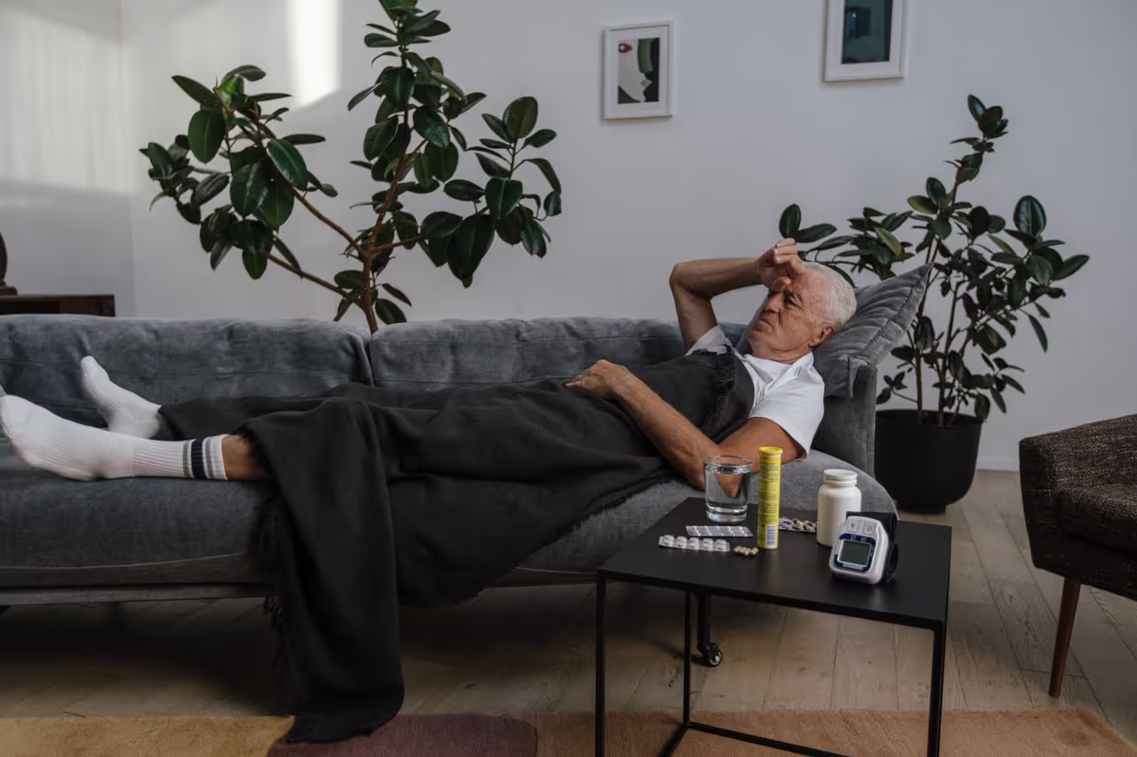 A person sick laying on the couch with medicine around him A person sick laying on the couch with medicine around him