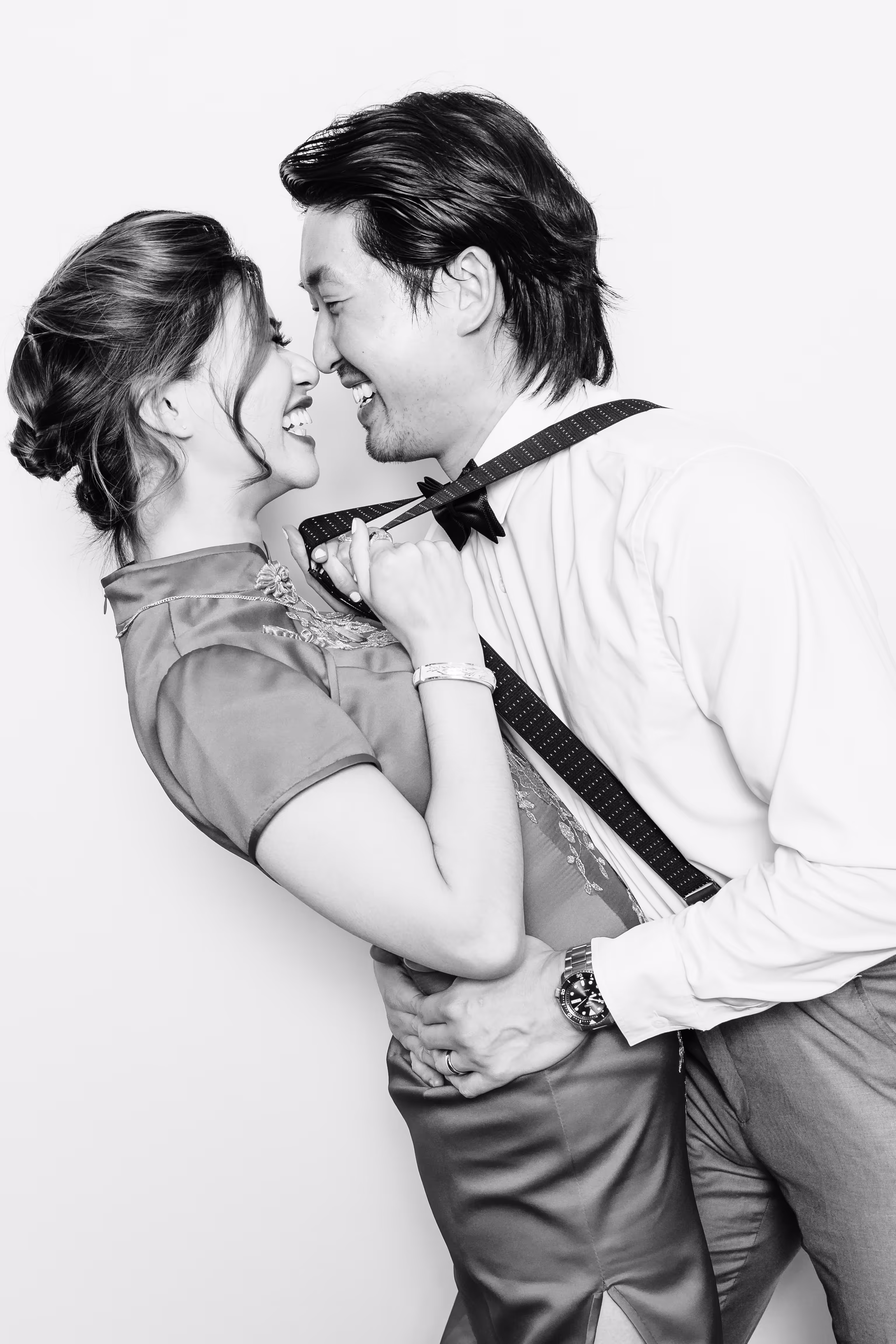 A couple facing each other while the wife holds on to her husband's suspenders while leaning back in a black & white photo