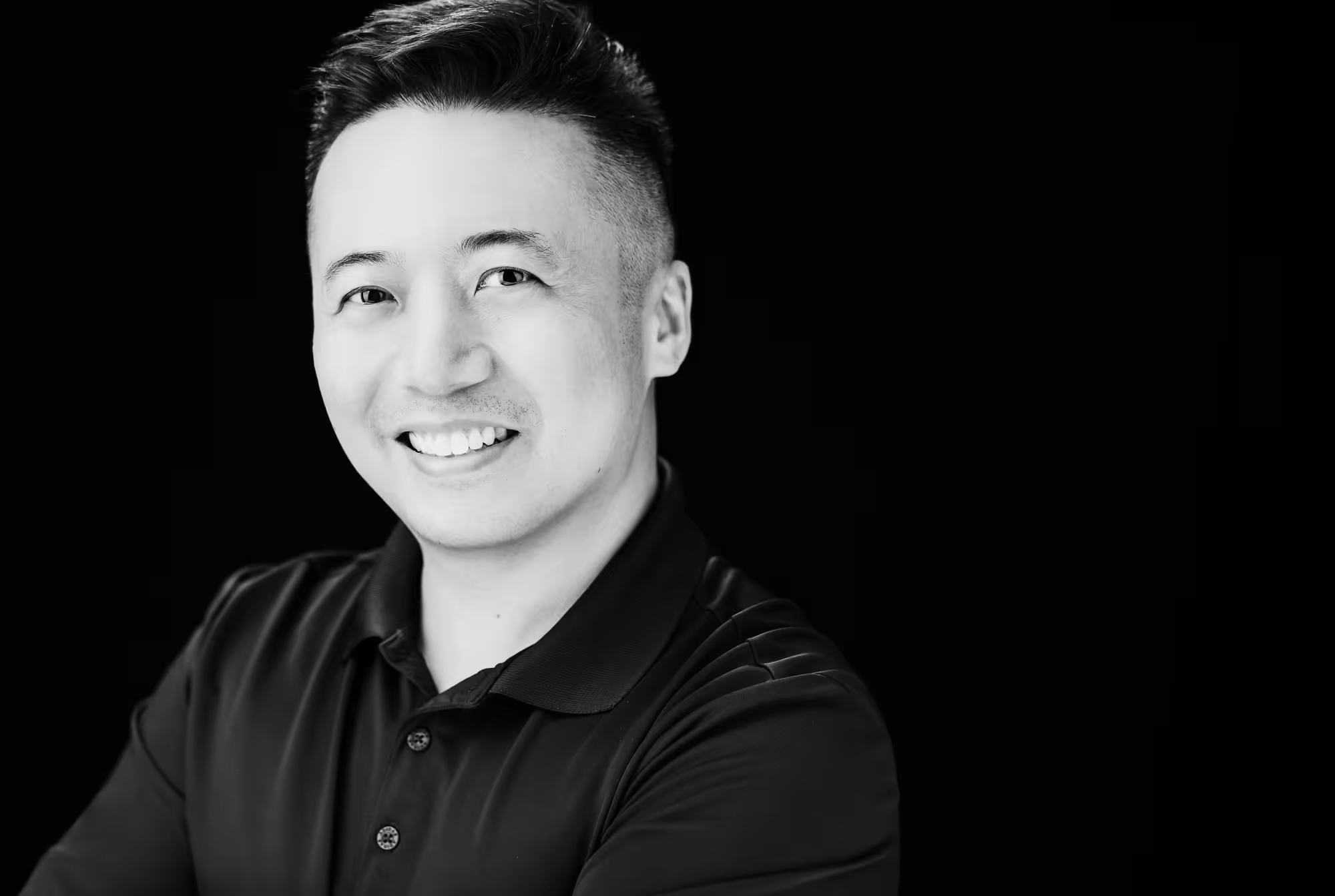 Black and white image of an Asian male facing the camera wearing a golf polo shirt while smiling.
