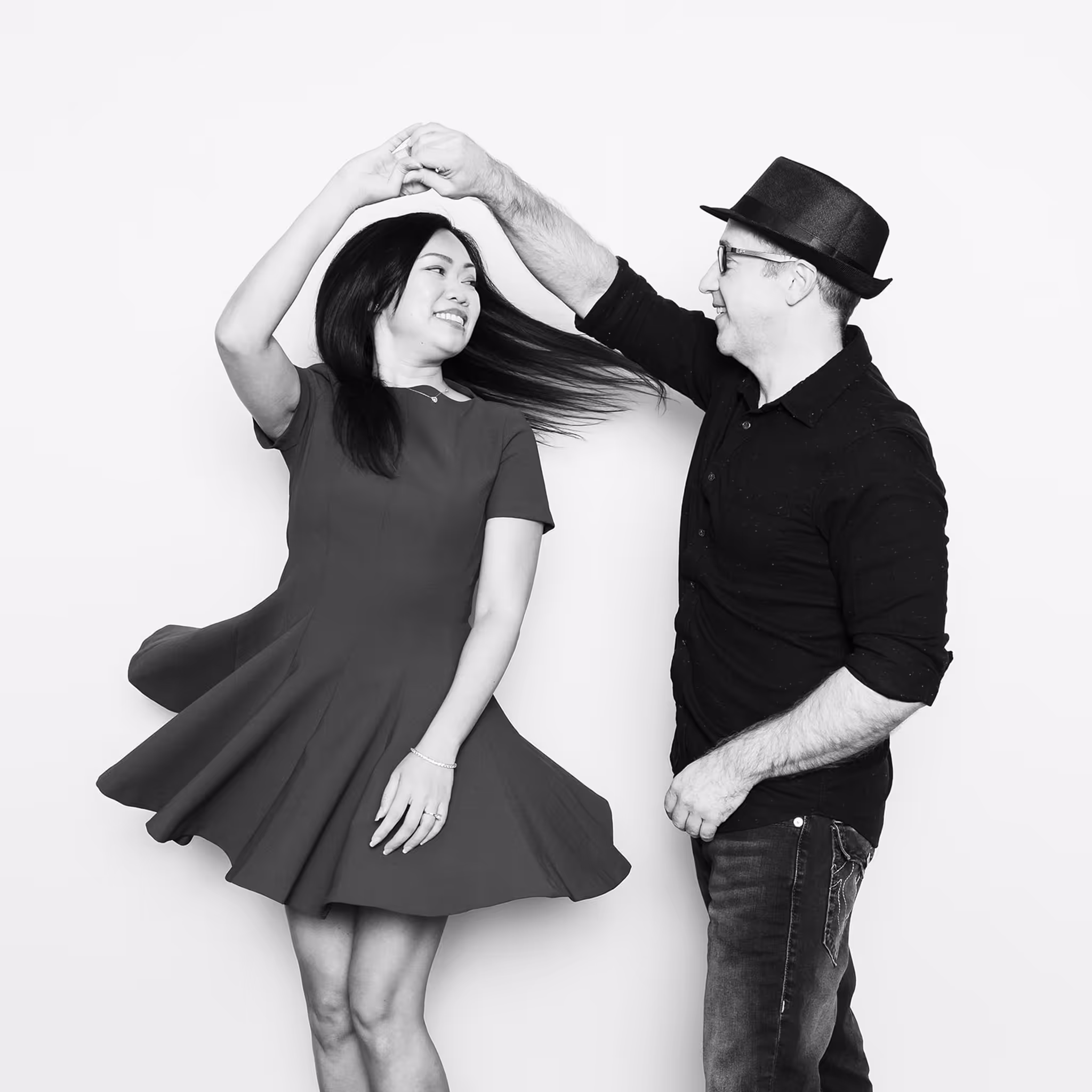 A couple twirling in a dance move in front of a Black and White Portrait Station allowing her dress to flair along with her hair