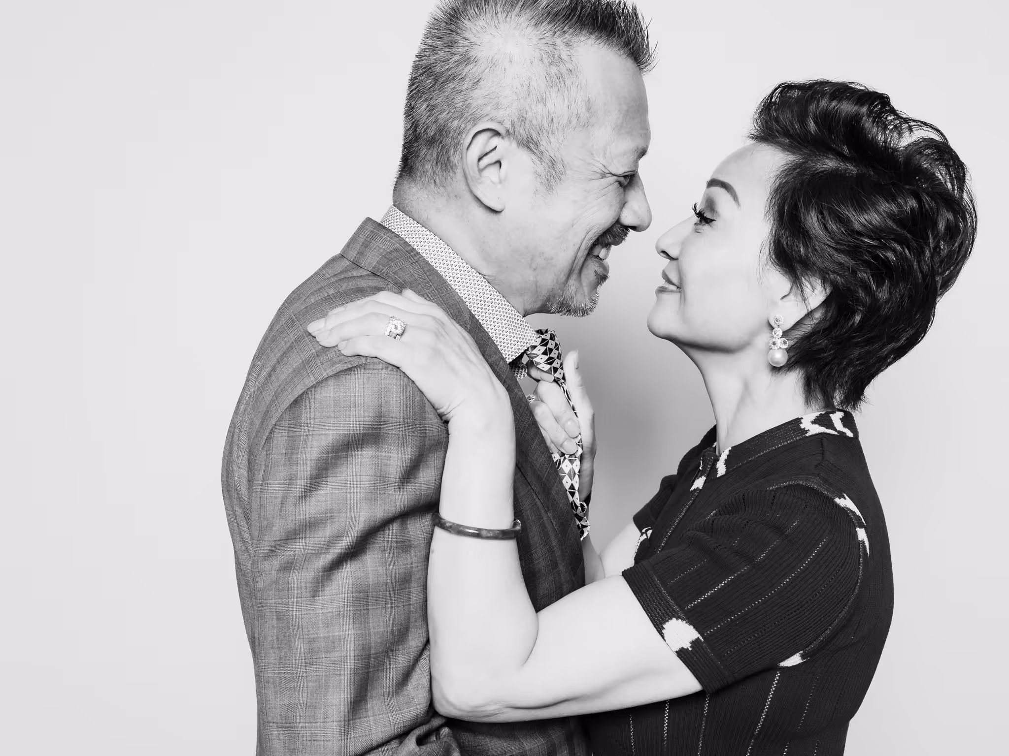 Elder Asian couple facing each other while the wife holds onto the tie of her husband while smiling to each other at a Black and White Wedding Photography Studio in Vancouver