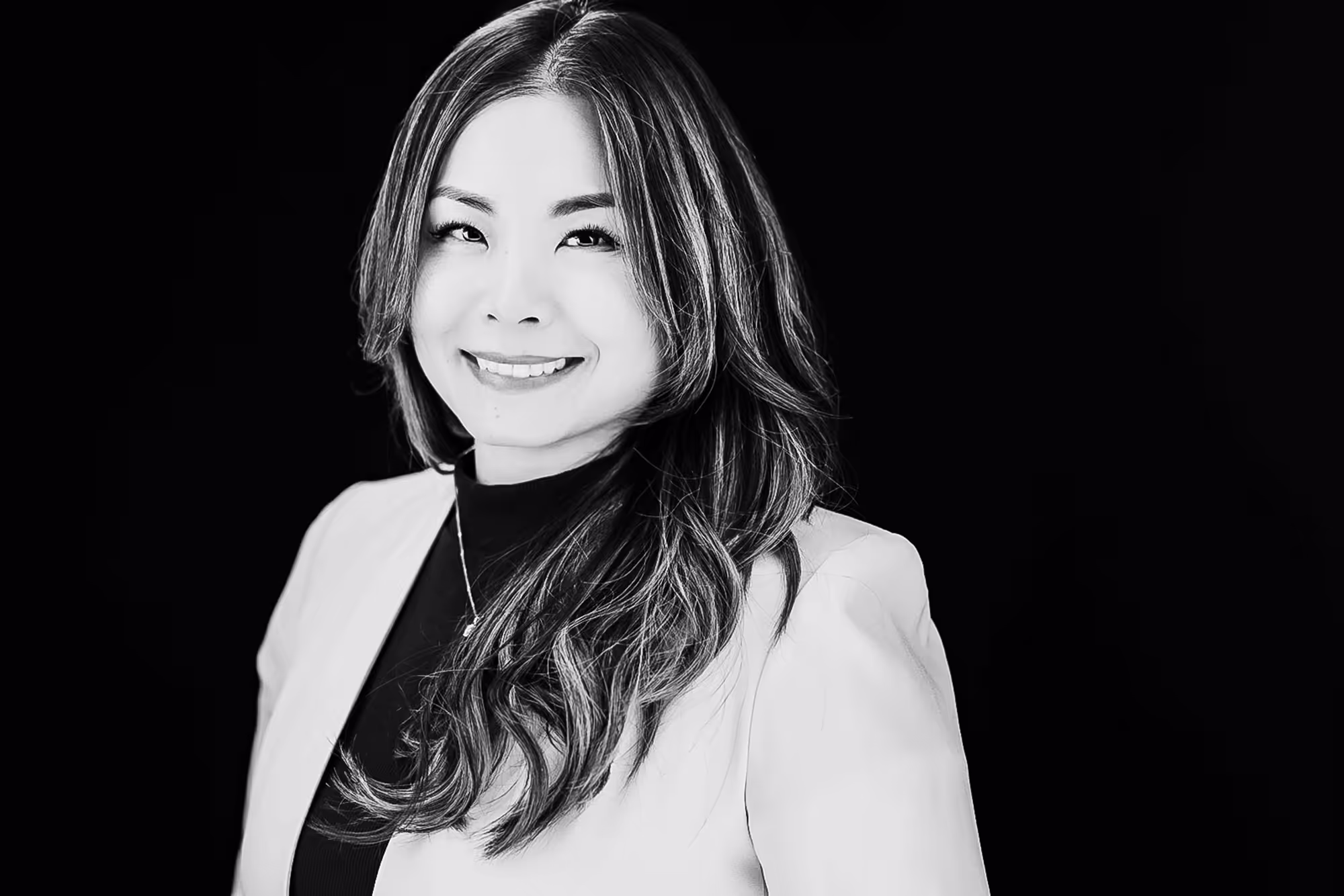 Black & White photo of an Asian female wearing a blazer and facing the camera while holding a smile.